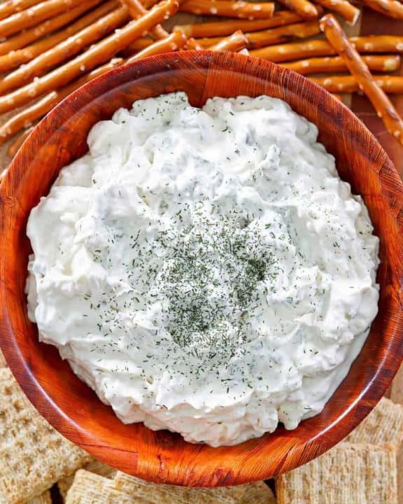 a bowl of dill pickle dip, pretzel sticks, and crackers