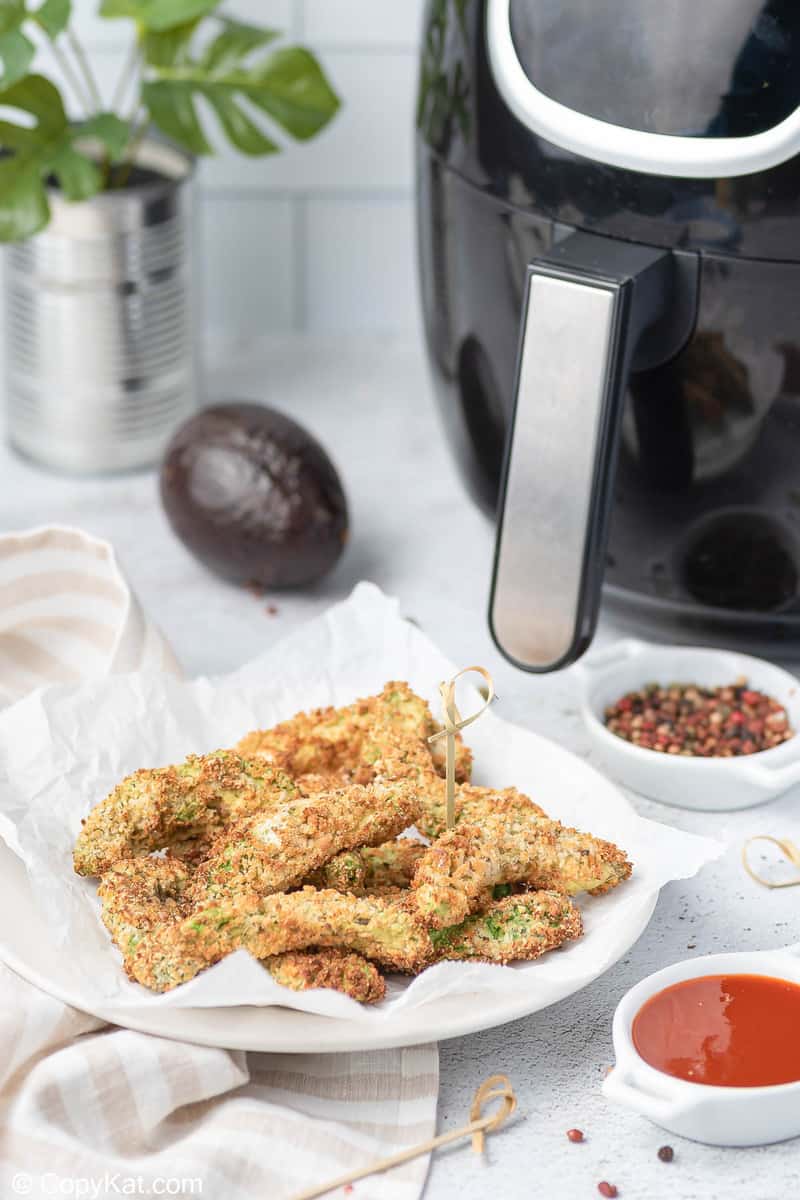 avocado fries on a plate next to an air fryer