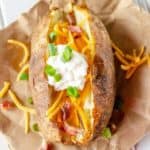 air fryer baked potato topped with butter, cheese, sour cream, bacon, and chives