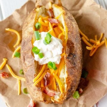 air fryer baked potato topped with butter, cheese, sour cream, bacon, and chives