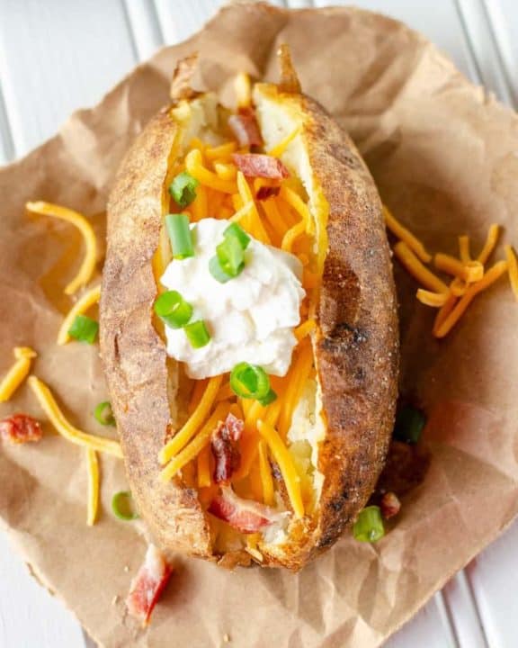 air fryer baked potato topped with butter, cheese, sour cream, bacon, and chives