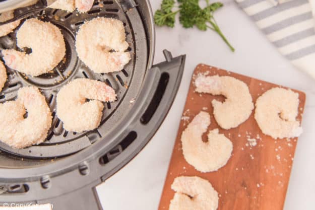 panko breaded shrimp in an air fryer and on a board