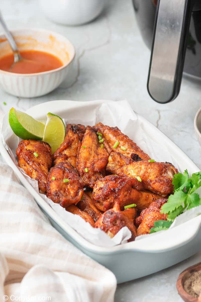 air fryer sweet and spicy chicken wings in a serving dish and a bowl of wing sauce