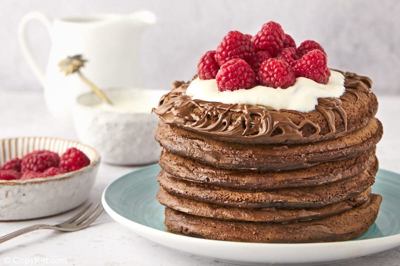 a stack of six chocolate pancakes, raspberries, cream, and a small pitcher