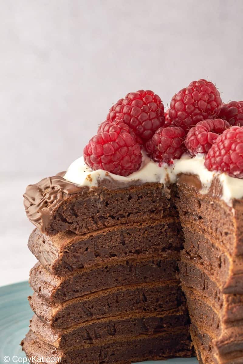 stack of chocolate pancakes with raspberries and whipped cream with slice cut out