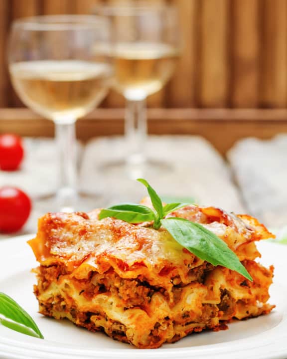 homemade lasagna on a plate and two glasses of white wine