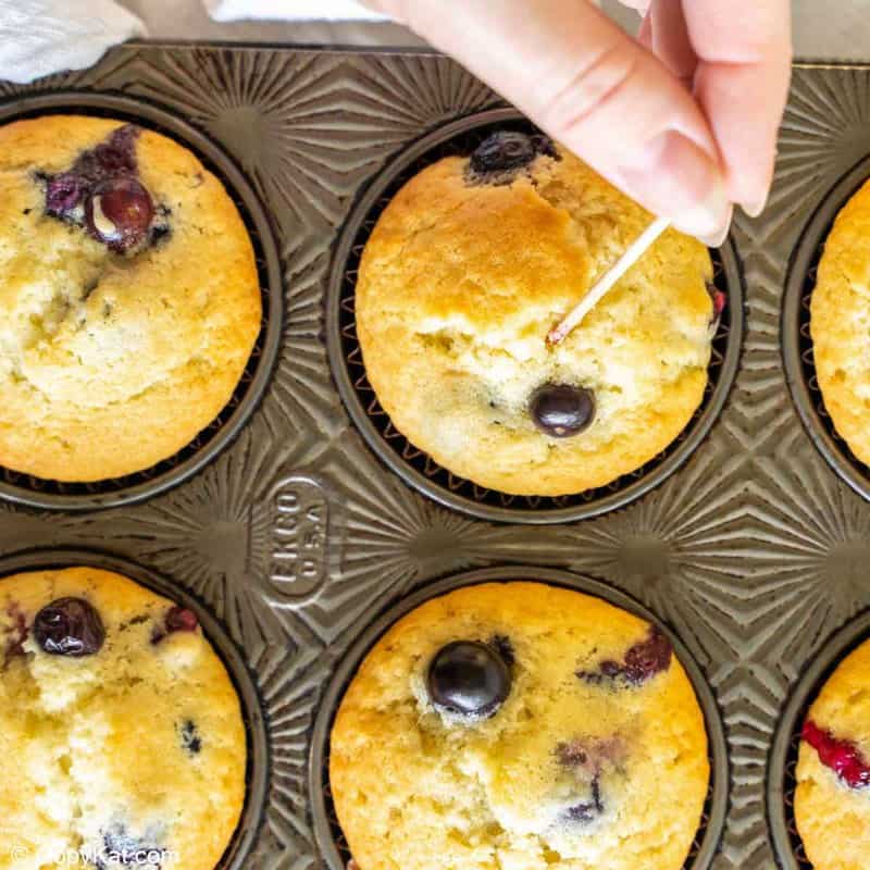 inserting a toothpick in a blueberry muffin to test for doneness