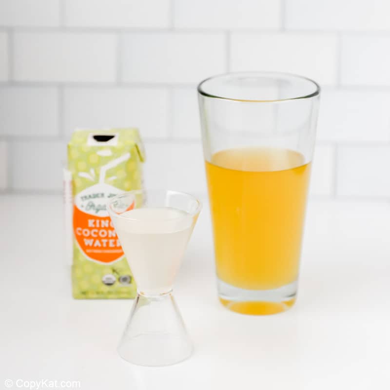 adding coconut water to a cocktail shaker with wine and pineapple juice