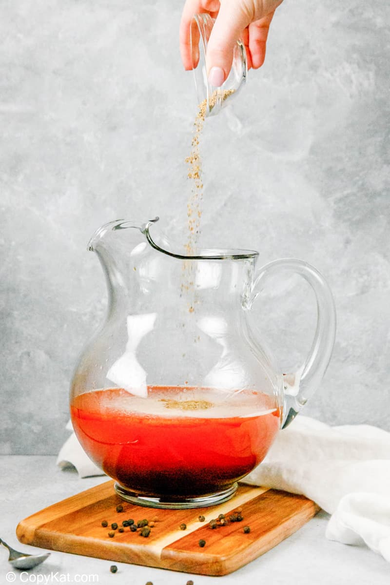 pouring celery salt and black pepper into a pitcher of homemade bloody mary mix