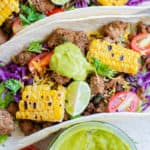ground beef taco with lettuce, cabbage, onion, tomato, corn, guacamole, and lime