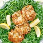 overhead view of four Maryland crab cakes and lemon wedges on top of arugula