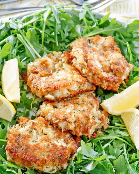 four Maryland crab cakes, lemon wedges, and arugula on a platter