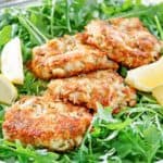 four Maryland crab cakes and lemon wedges on top of arugula