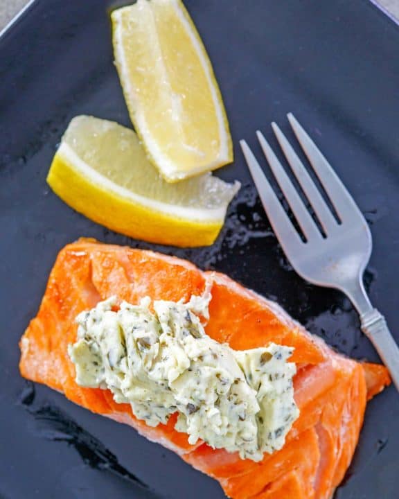 overhead view of salmon with pesto cream cheese sauce and two lemon wedges on a plate