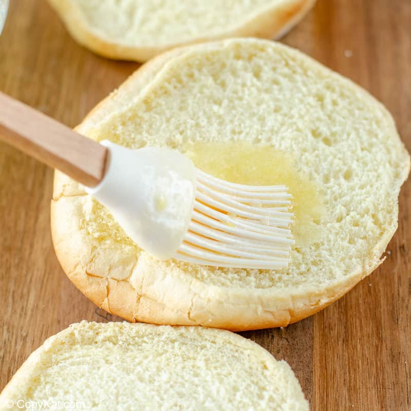 spreading garlic butter sauce on a hamburger bun.
