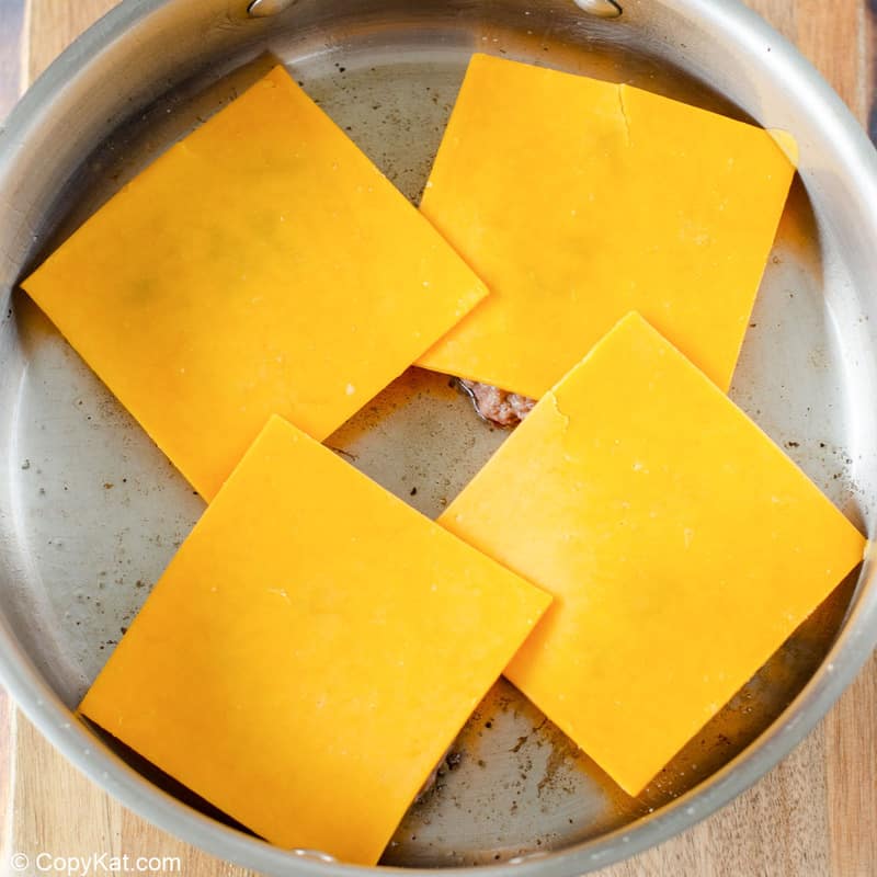 cheese on top of ground beef patties in a skillet.