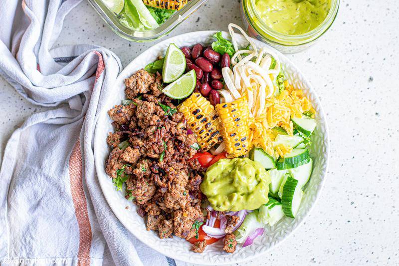 ground beef taco bowl with cheese, guacamole, beans, and vegetables