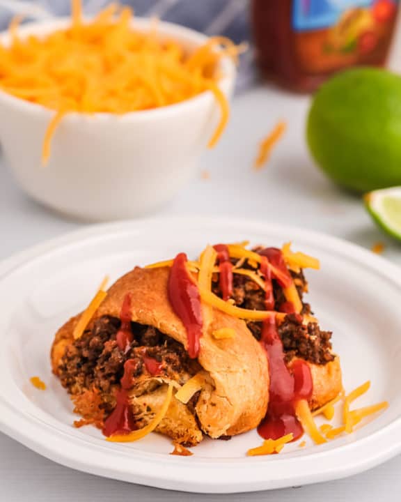 piece of a taco ring on a plate and a bowl of shredded cheese