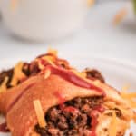 piece of a taco ring topped with taco sauce and cheese on a plate
