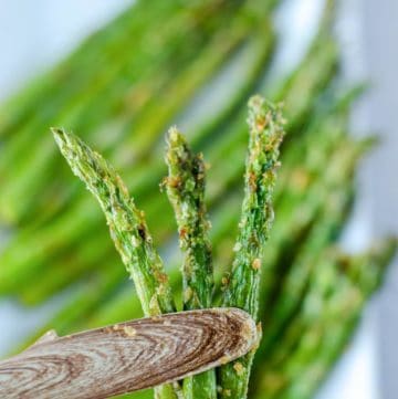three air fried asparagus spears held by tongs