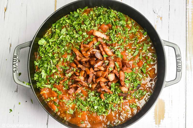 adding bacon and cilantro to tomato sauce for huevos rancheros