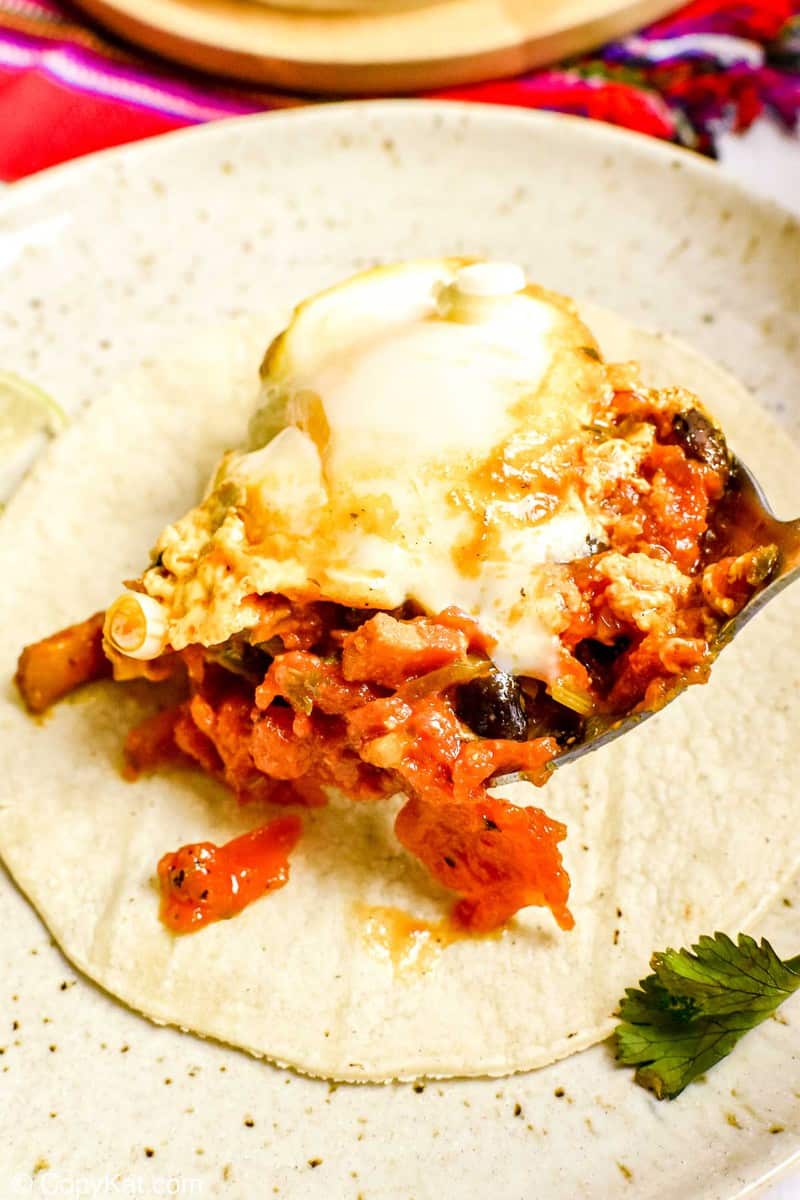spooning huevos rancheros on a corn tortilla
