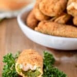jalapeno popper with a bite taken out of it in front of a bowl of poppers