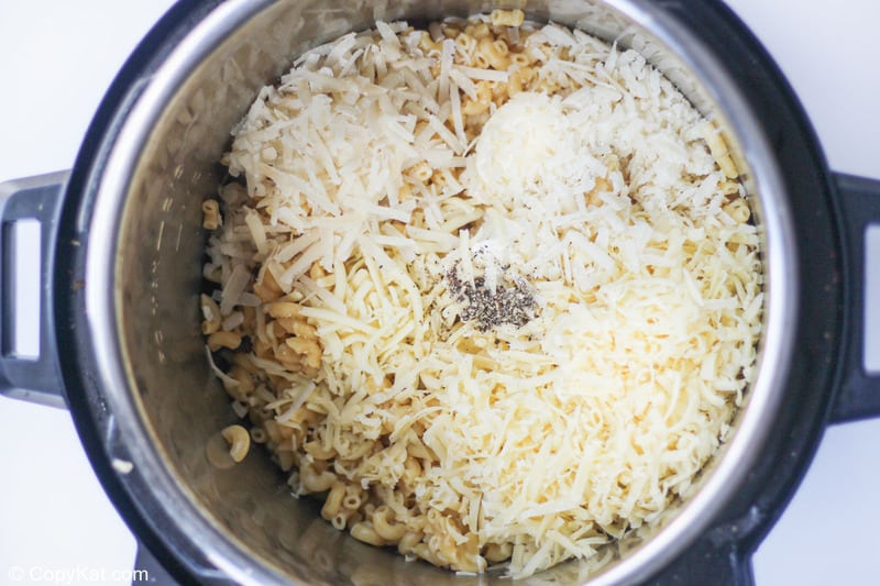 adding cheeses and seasoning to macaroni in an Instant Pot