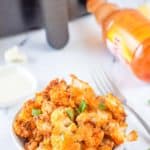 a bowl of buffalo cauliflower in front of an air fryer