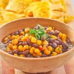 a bowl of black bean and corn salad and corn tortilla chips on a platter