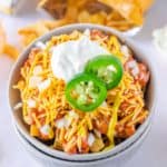Frito Pie topped with onions, sour cream, and jalapeno pepper slices