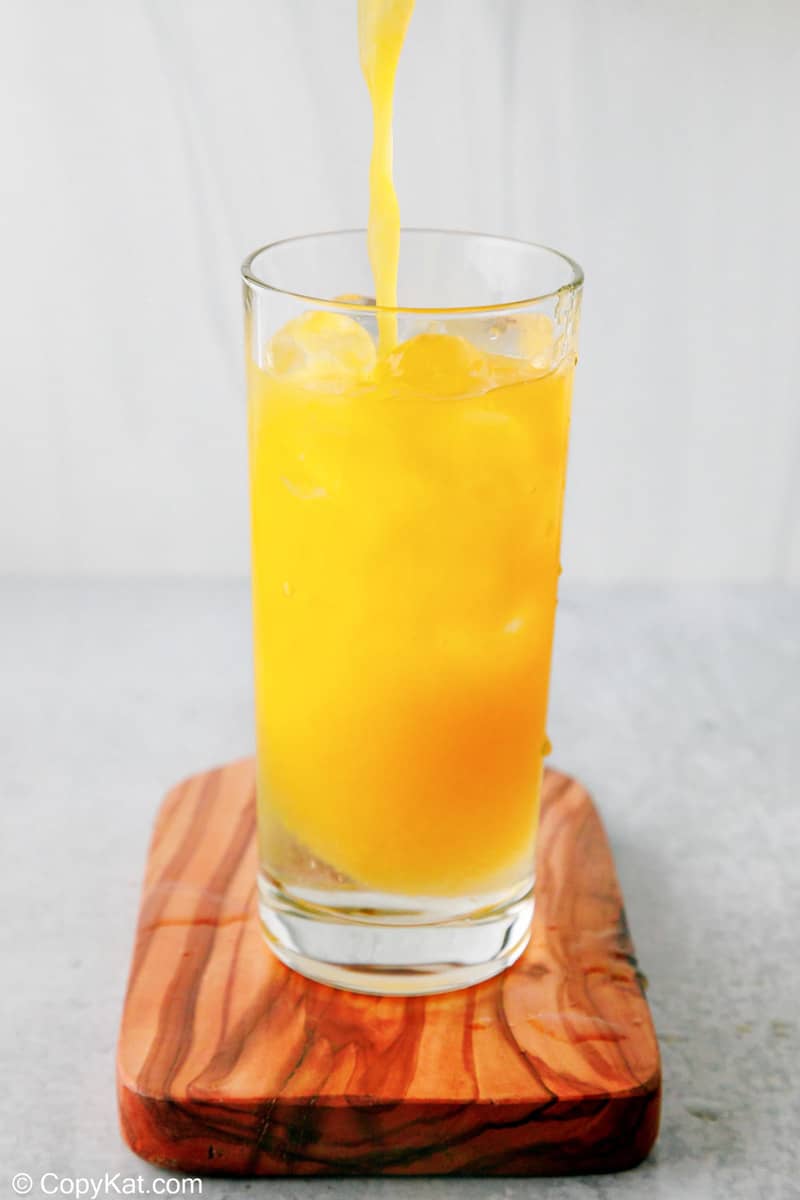 adding orange juice to peach schnapps and ice in a glass