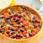 a bowl of homemade Panera black bean soup, a spoon, and half of a lemon