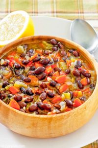a bowl of homemade Panera black bean soup, a spoon, and half of a lemon