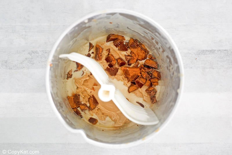 adding peanut butter cups to ice cream in an ice cream maker
