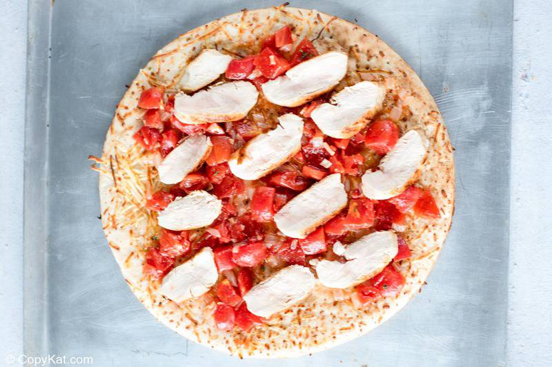 pizza crust topped with tomatoes and chicken