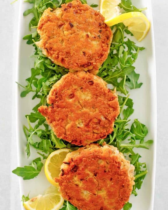 three salmon patties, lemon slices, and arugula on a platter
