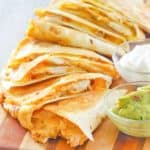 homemade Taco Bell chicken quesadilla, sour cream, and guacamole on a board