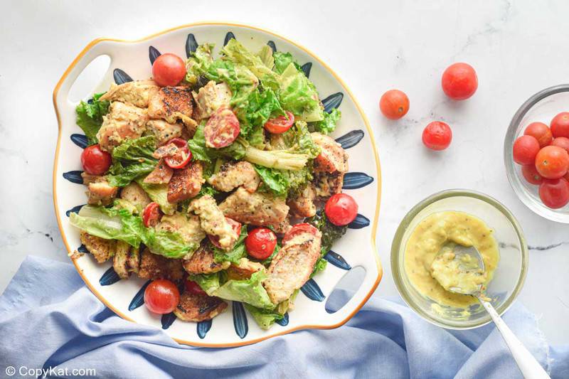 chicken caesar salad, bowl of dressing, and cherry tomatoes