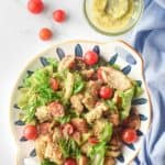 overhead view of chicken Caesar salad, dressing, and tomatoes