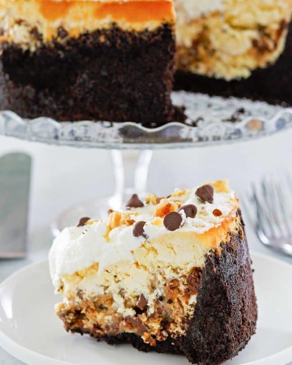 cookie dough cheesecake slice on a plate and the cheesecake on a stand