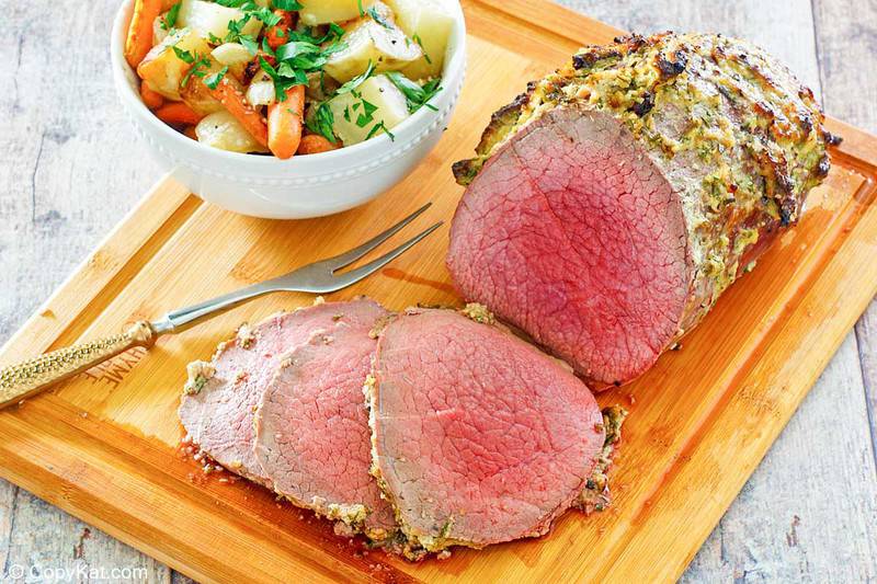eye of round roast, roast slices, bowl of vegetables, and meat fork on a cutting board
