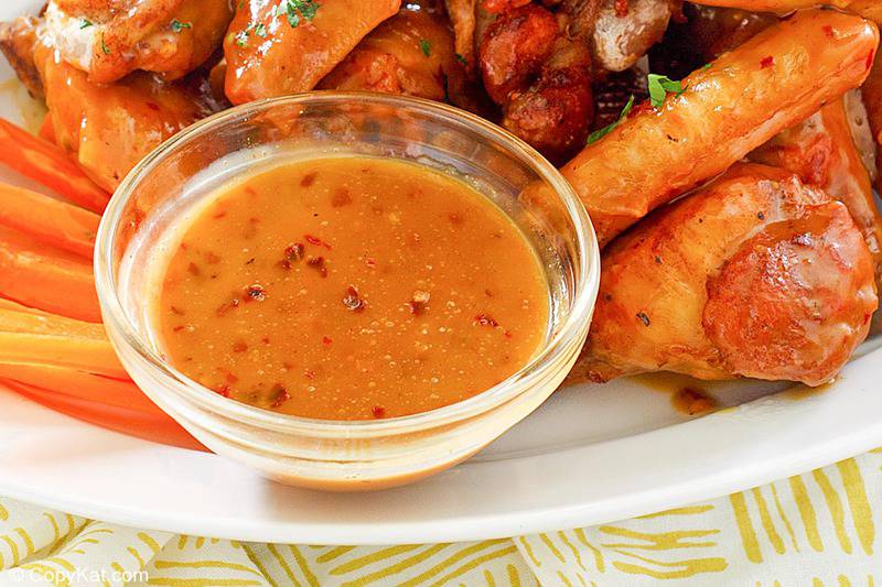 a bowl of mustard bbq sauce on a plate with wings and carrot sticks