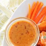 a bowl of mustard bbq sauce, carrot sticks, and wings on a platter