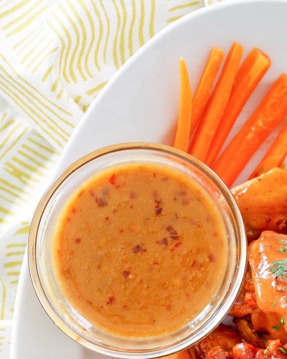 a bowl of mustard bbq sauce, carrot sticks, and wings on a platter