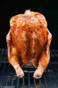 seasoned chicken on a beer can chicken holder in a smoker