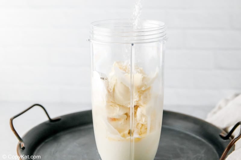 adding banana pudding mix into a blender for a banana milkshake