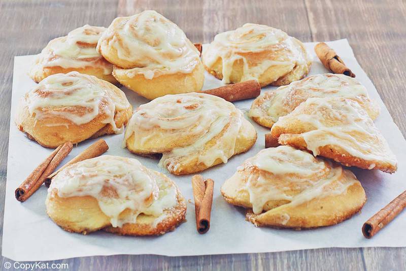 frosted cinnamon rolls and cinnamon sticks on parchment paper