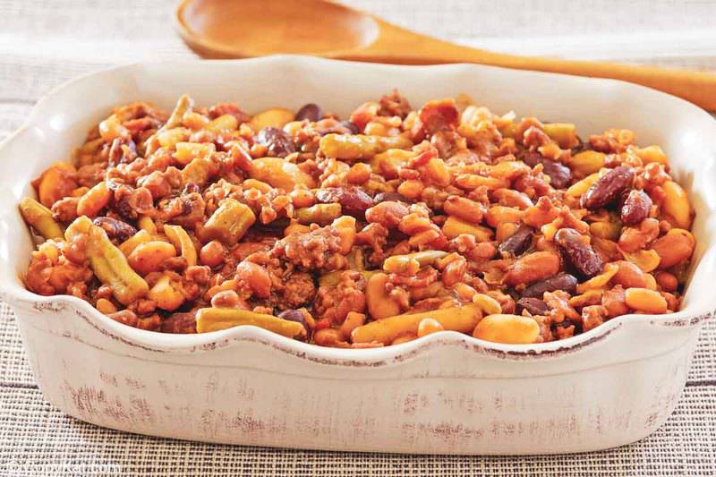 calico beans in a dish with a wooden spoon behind it