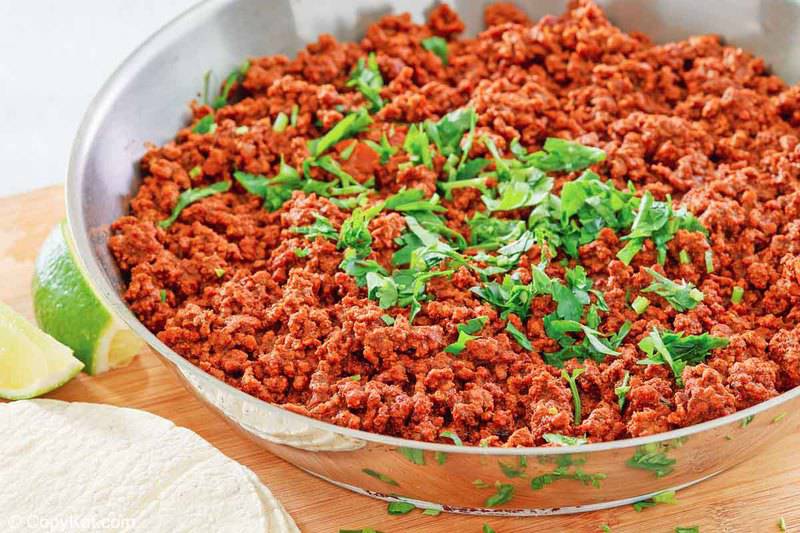 chili colorado con carne in a skillet, flour tortillas, and lime wedges